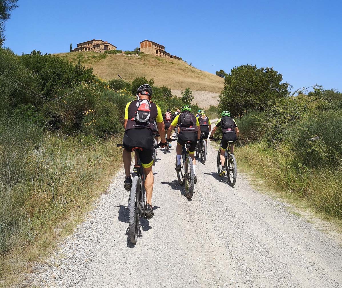 Mountainbikers rijden toertocht op brede gravelweg in heuvelachtig landschap