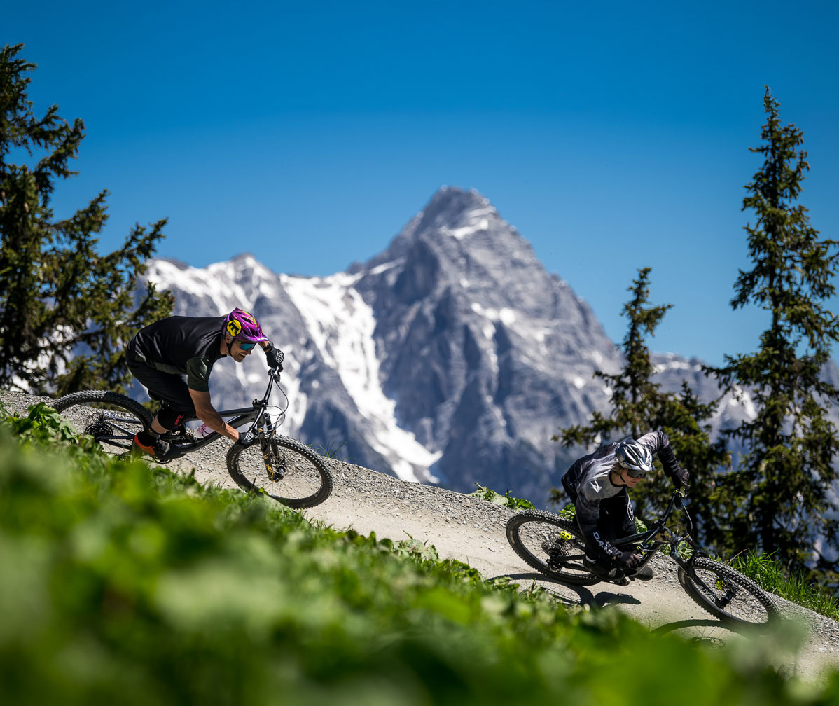 Two mountain bikers ride a technical enduro descent on an alpine trail during enduro training